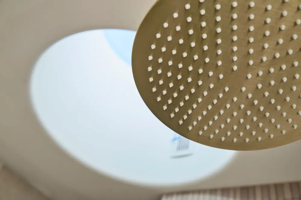 Close-up of a gold rainfall showerhead with multiple water nozzles, mounted on a white ceiling.