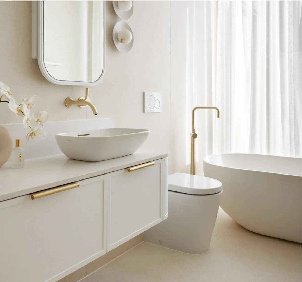 Modern white bathroom with vessel sink, brass fixtures, freestanding tub, and white orchids on vanity.