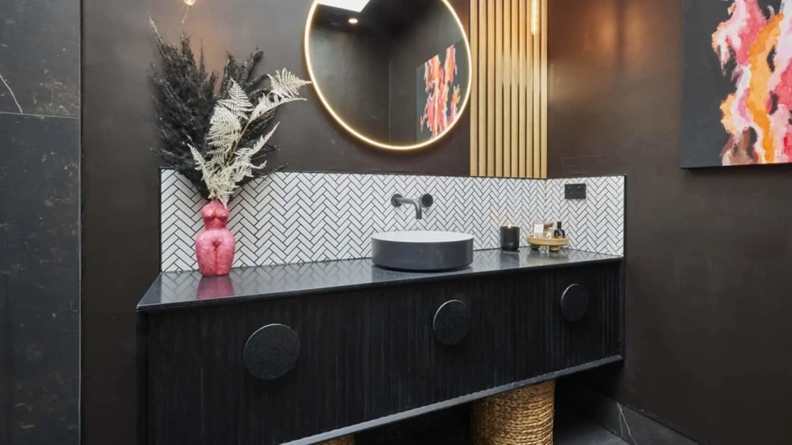 Modern bathroom with dark vanity, herringbone tile backsplash, round mirror, and pink vase with dried plants.