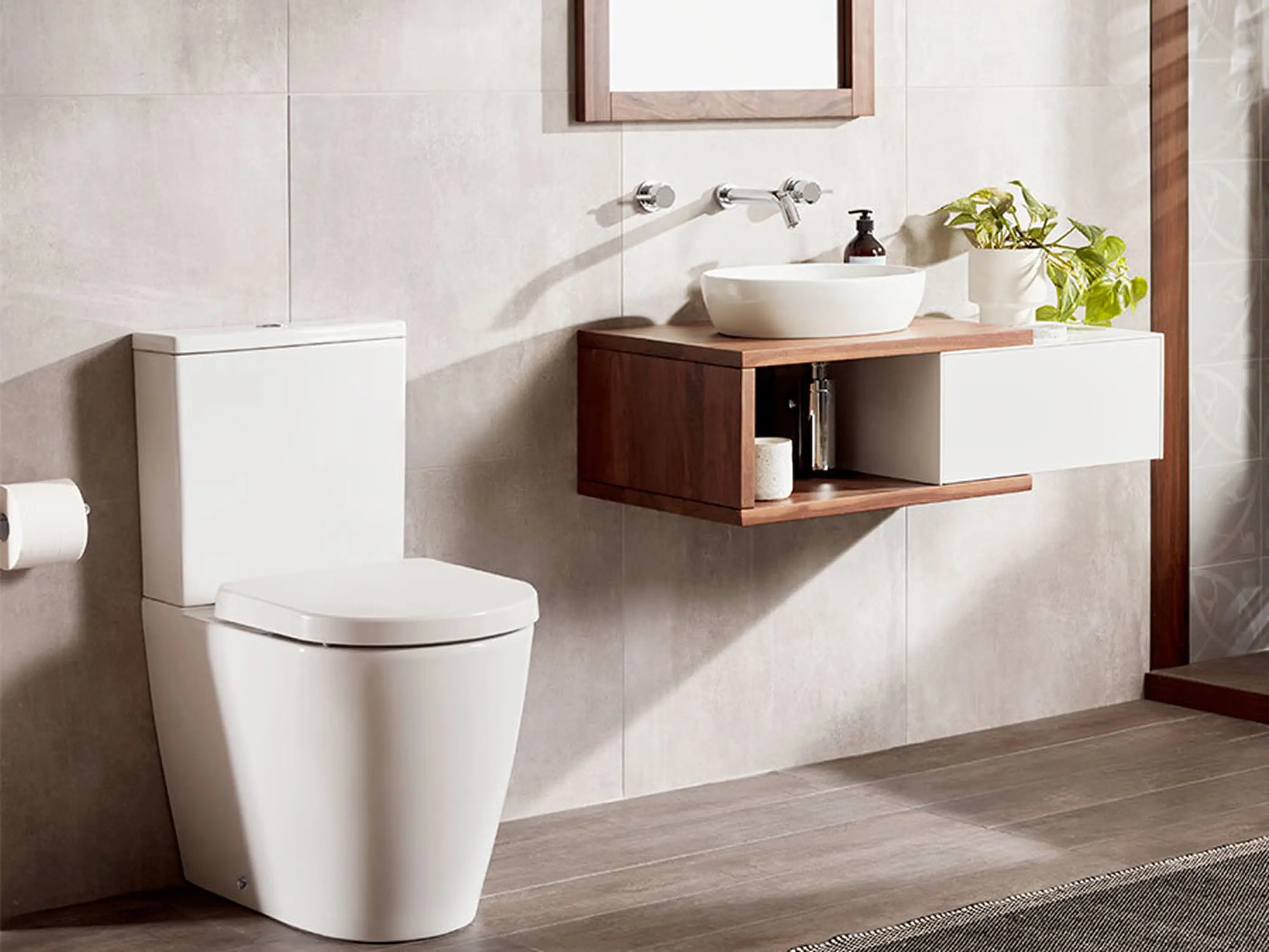 Modern bathroom with white toilet, floating wooden vanity with vessel sink, wall-mounted faucet, and small green plant.