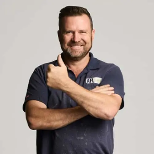 Person in navy polo shirt giving thumbs up against light background, smiling confidently.