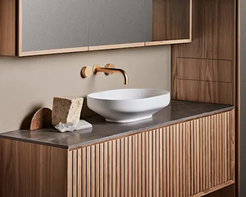 Modern bathroom vanity with white vessel sink, brass wall-mounted faucet, and wooden cabinetry with gray countertop.