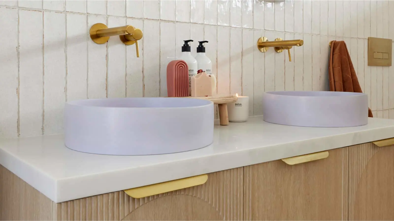 Modern bathroom with two white circular vessel sinks, brass faucets, and toiletry products on a white countertop.