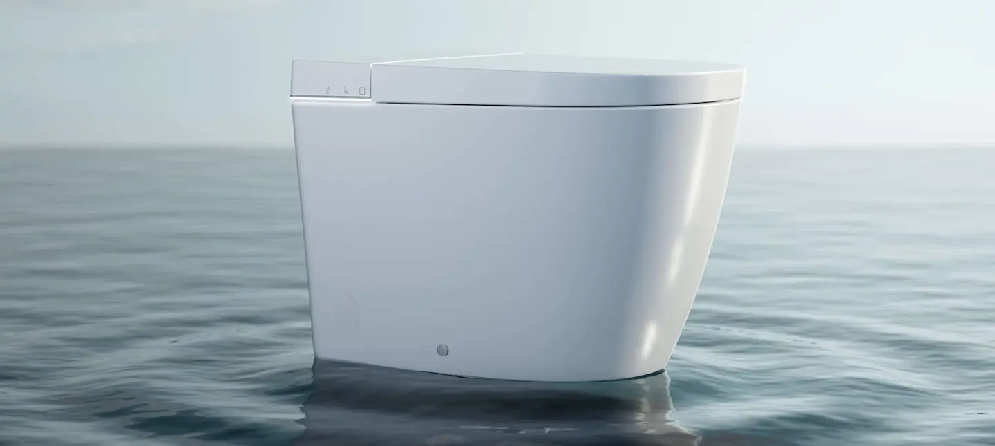 White one-piece smart toilet with a closed lid and control panel, shown against a calm water background.