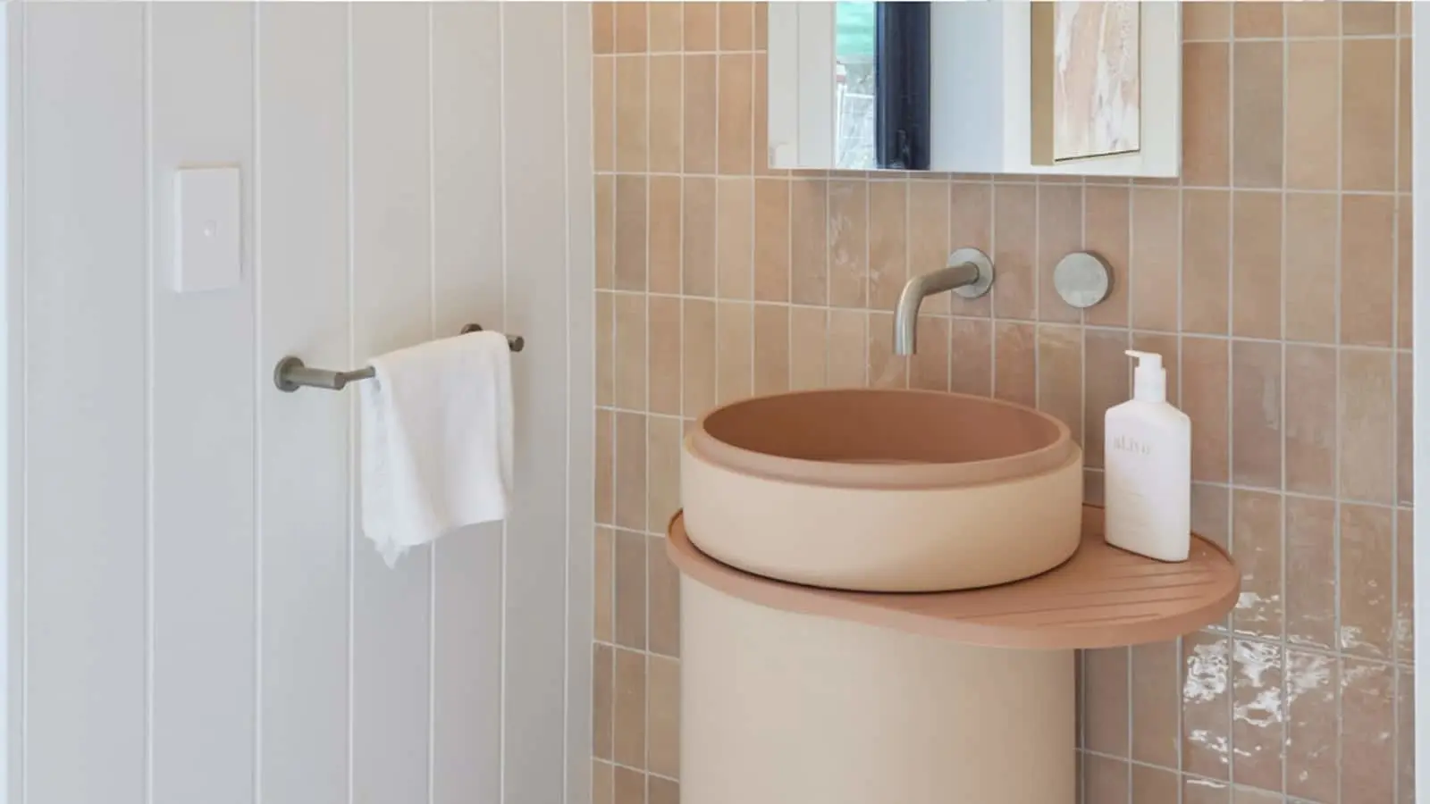 Modern bathroom with terracotta tiles, circular vessel sink on wooden shelf, wall-mounted faucet, and white towel rack.