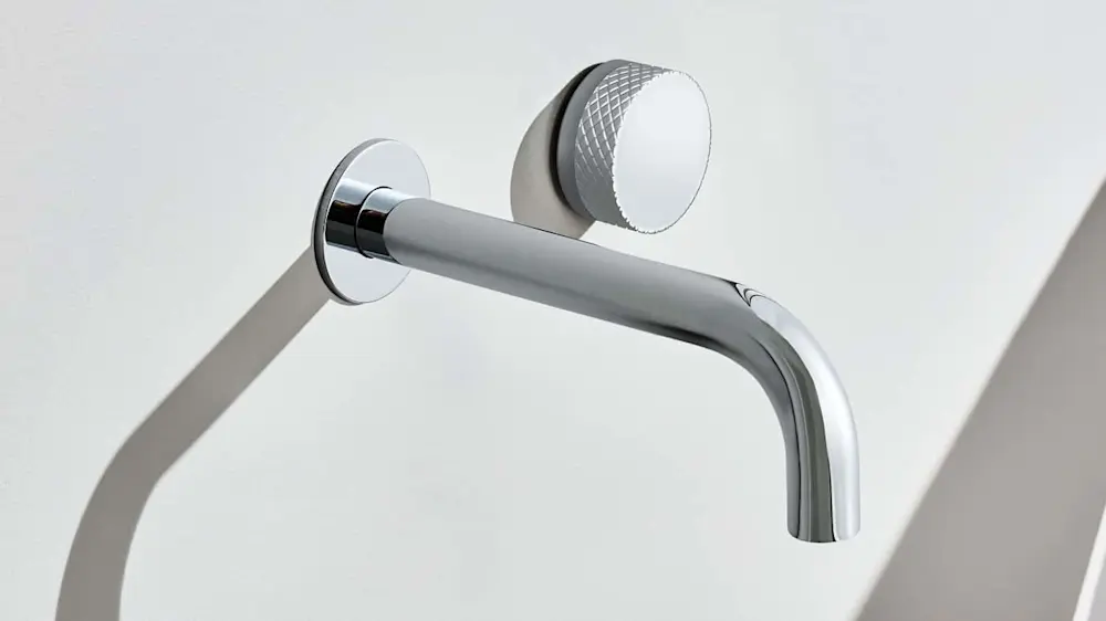 Modern chrome bathroom faucet with textured circular control knob mounted on a white wall.