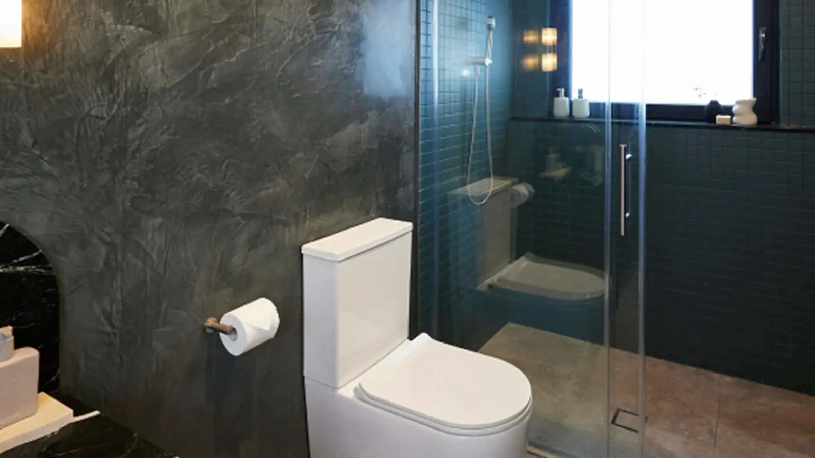 Modern bathroom with white toilet, textured gray walls, and glass shower enclosure with blue tiled interior.