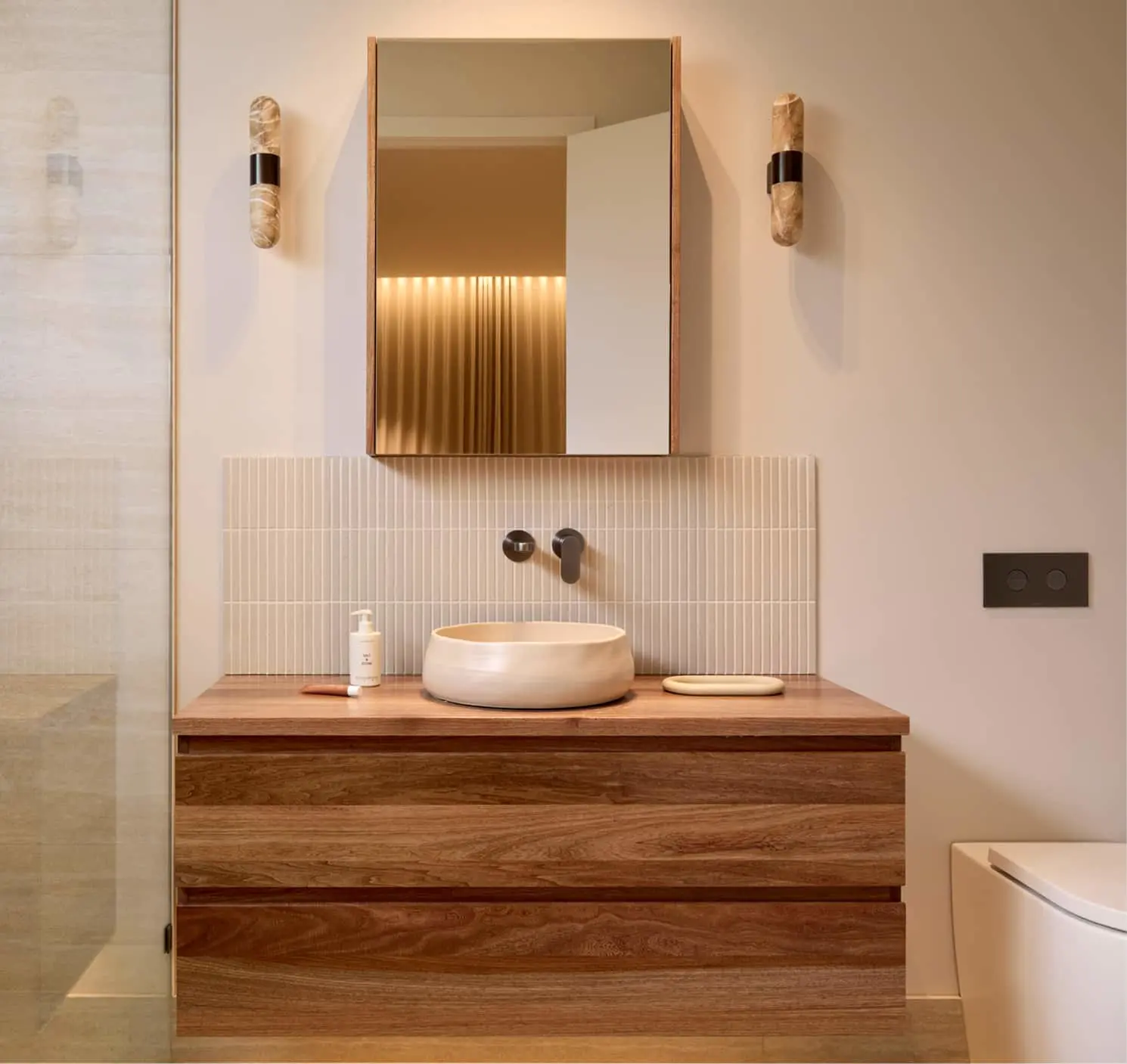 Modern bathroom vanity with wood cabinet, white vessel sink, wall-mounted faucet, and mirror with sconces.