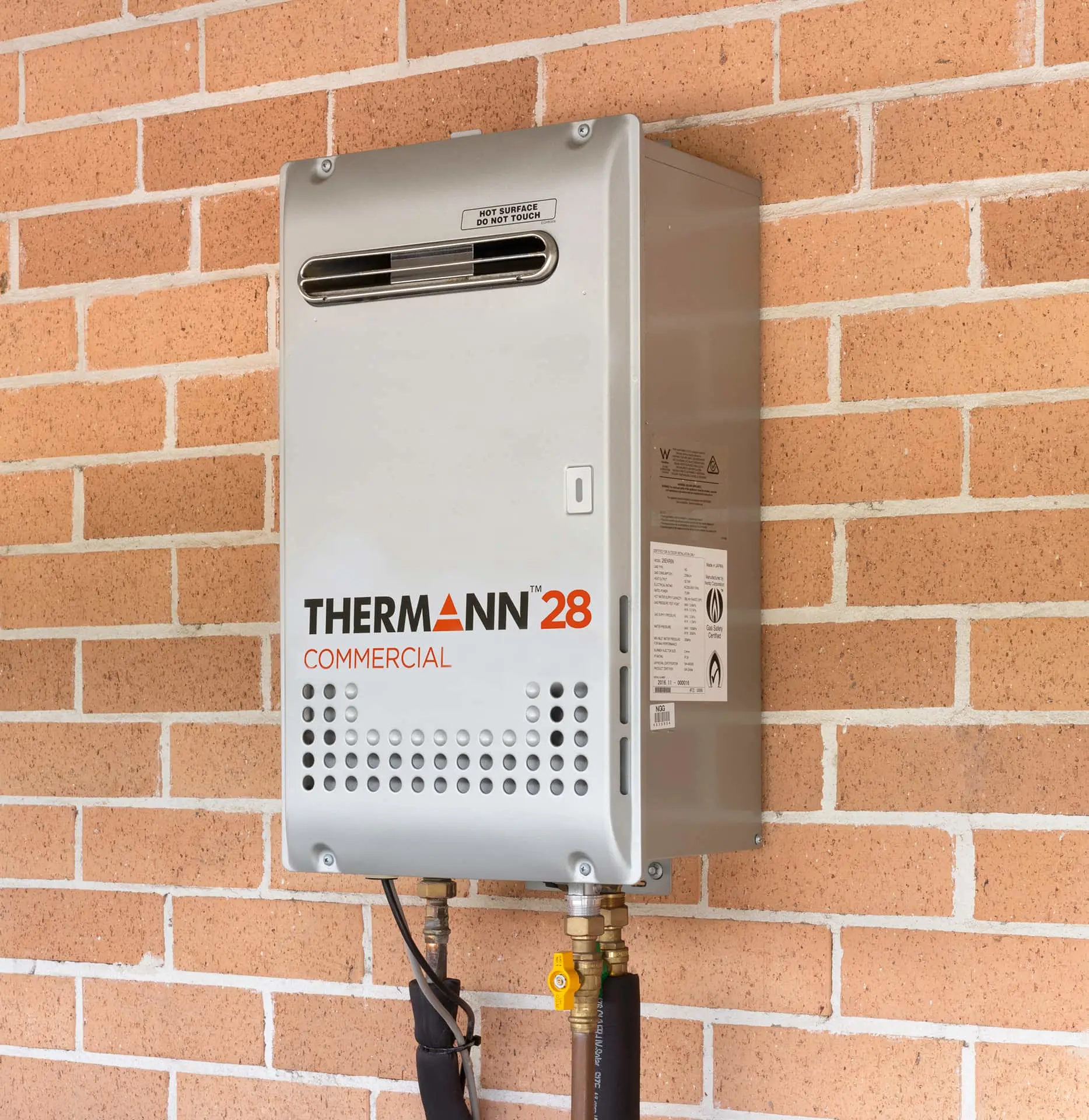 Thermann Commercial water heater mounted on brick wall with warning label and connected pipes.