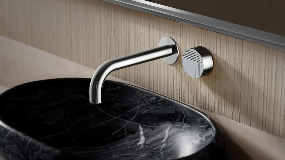 Modern wall-mounted chrome faucet with circular control knob above a black marble sink against light wood paneling.