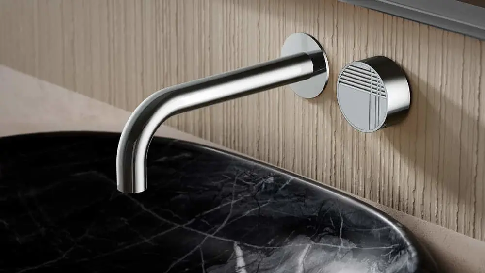 Modern wall-mounted chrome faucet with circular control knob above a black marble sink against light wood paneling.