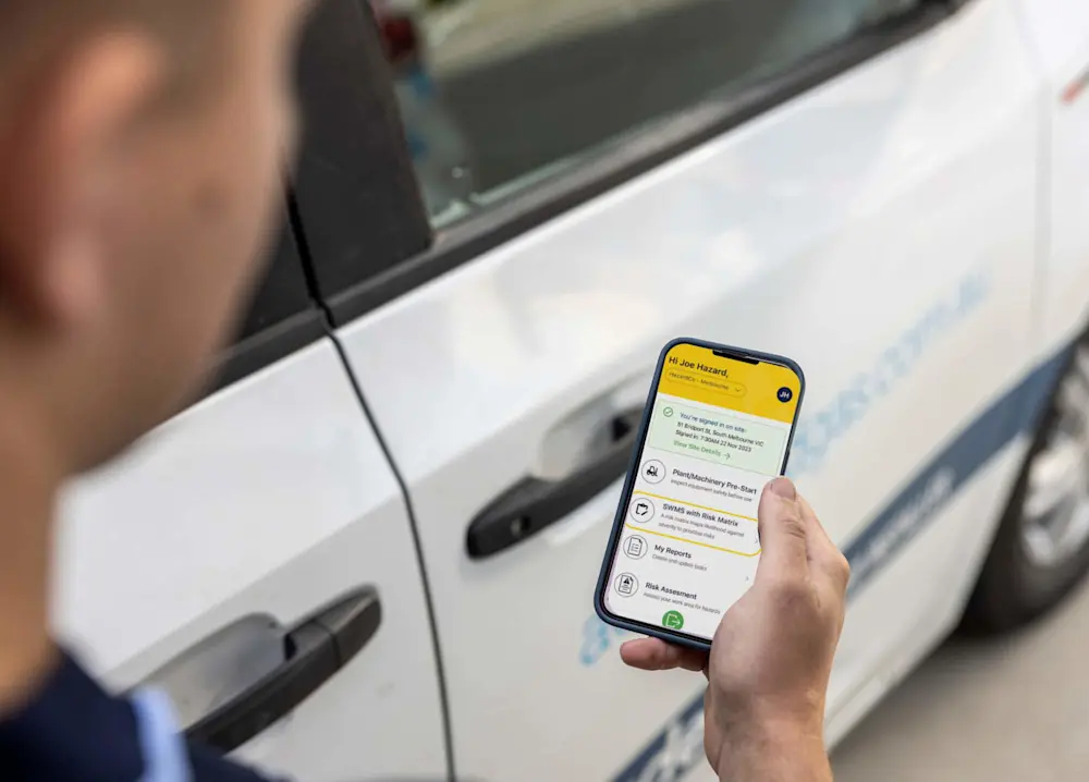 Hand holding smartphone displaying safety app with risk assessment features next to white service vehicle.
