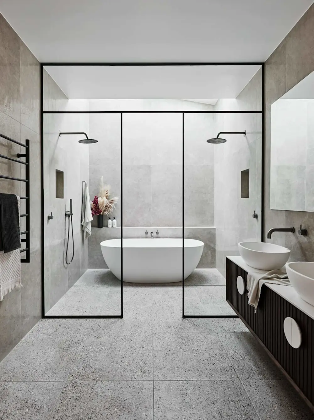 Modern bathroom with glass-enclosed shower area, freestanding white tub, dual sinks, and gray stone tile throughout.