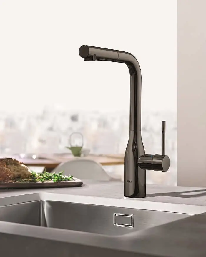 Modern black kitchen faucet with tall curved spout installed on stainless steel sink with food visible in background.