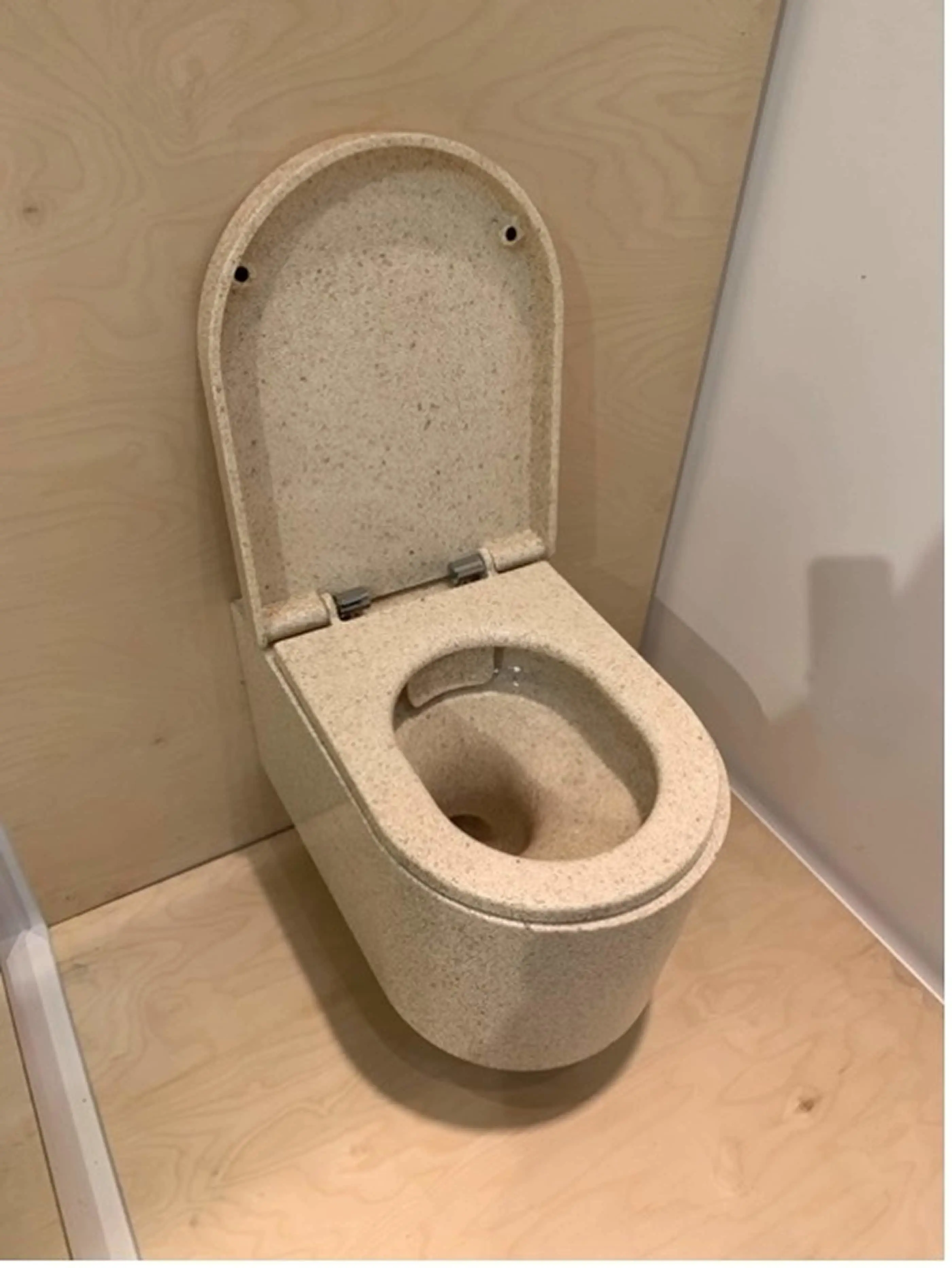 Beige stone-textured toilet with open lid in a bathroom with wooden walls and floor.