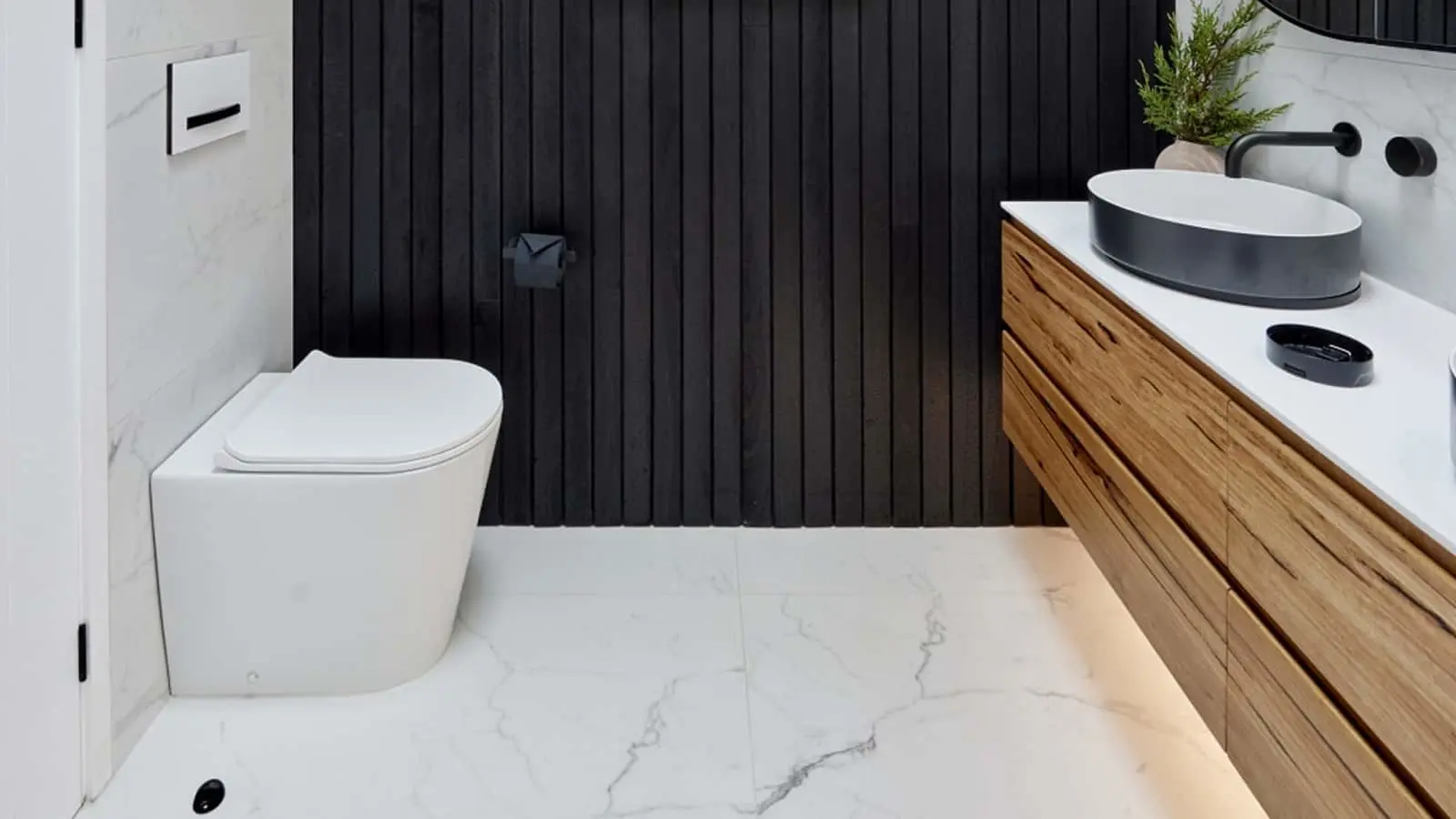Modern bathroom with black vertical wall panels, white toilet, wooden vanity with black basin, and marble floor.