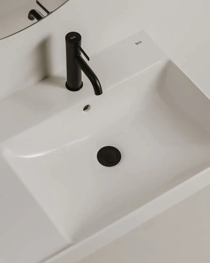 Modern white rectangular bathroom sink with matte black faucet and drain against a minimalist white countertop.