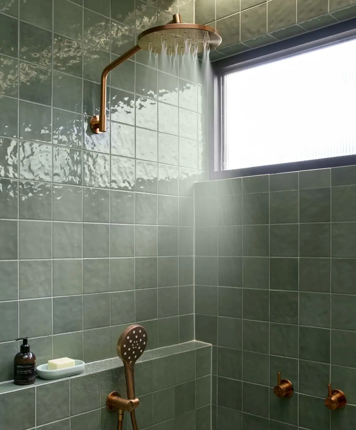 Modern bathroom with green tiles featuring bronze shower with rainhead.