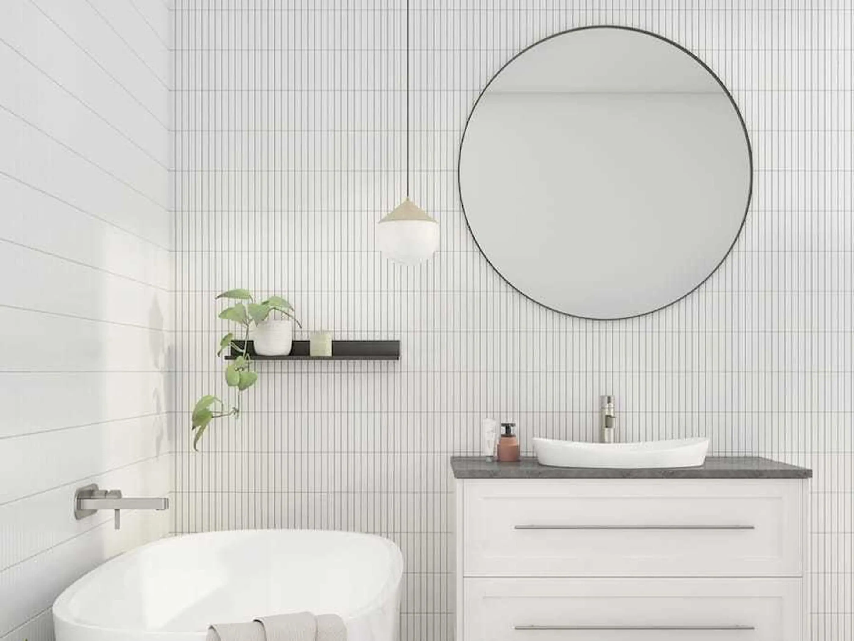 Modern white bathroom with round mirror, vessel sink, freestanding tub, pendant light, and small potted plant on shelf.