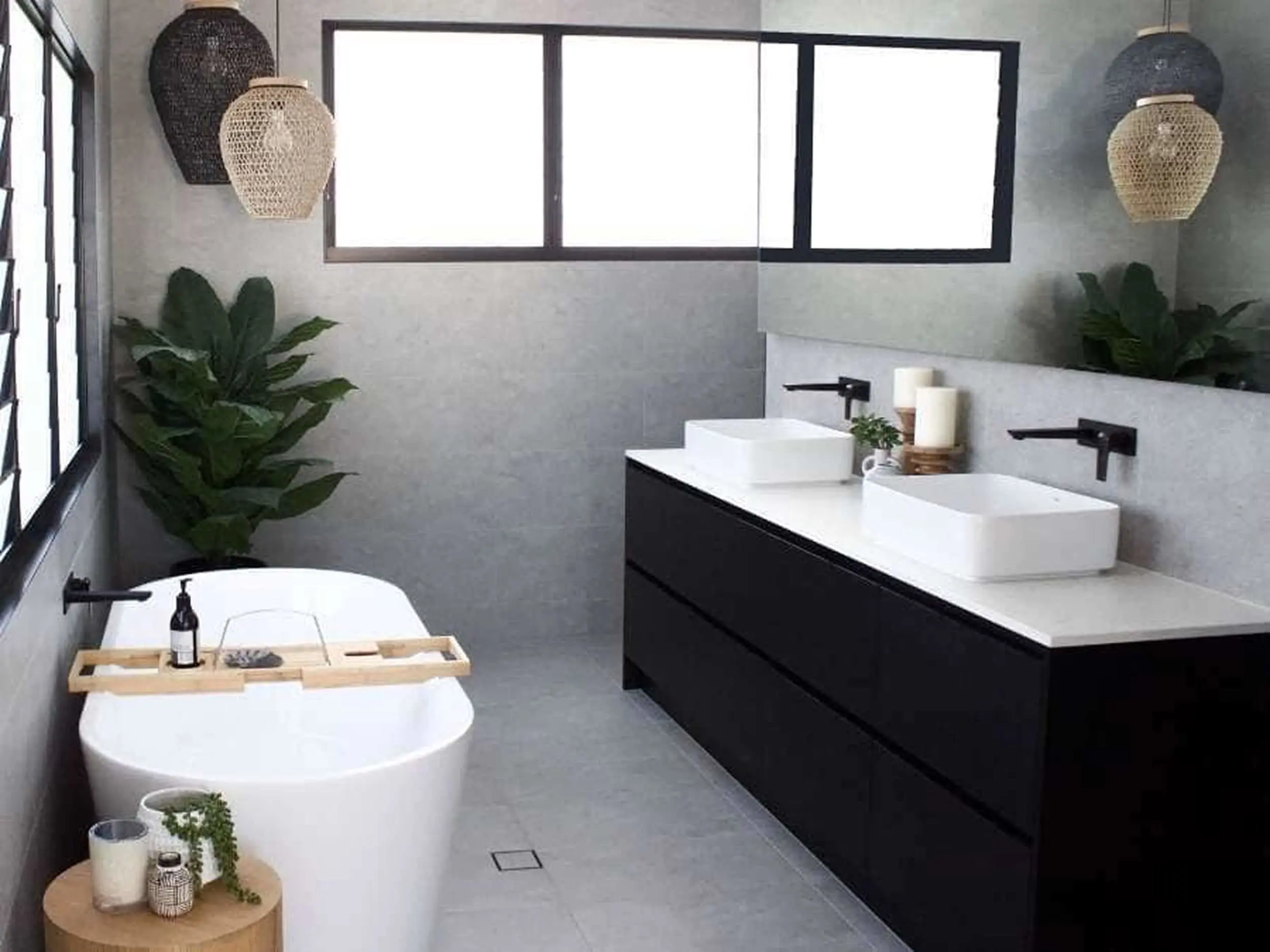 Modern bathroom with freestanding tub, black vanity with white sinks, woven pendant lights, and green plants.