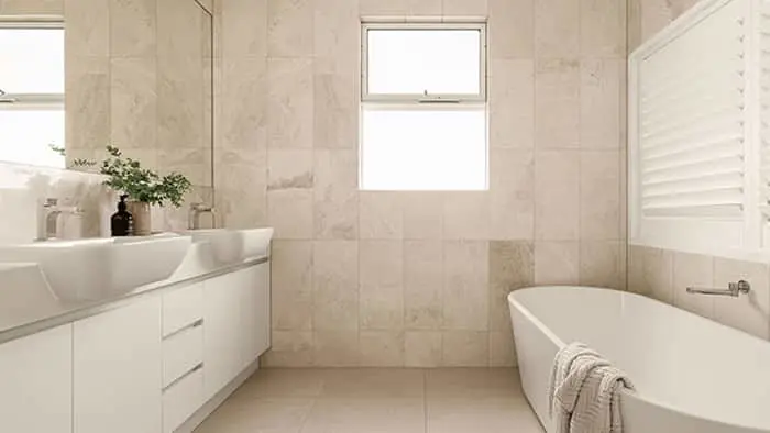 Modern bathroom with beige tile walls, white vanity, freestanding tub, and small window providing natural light.