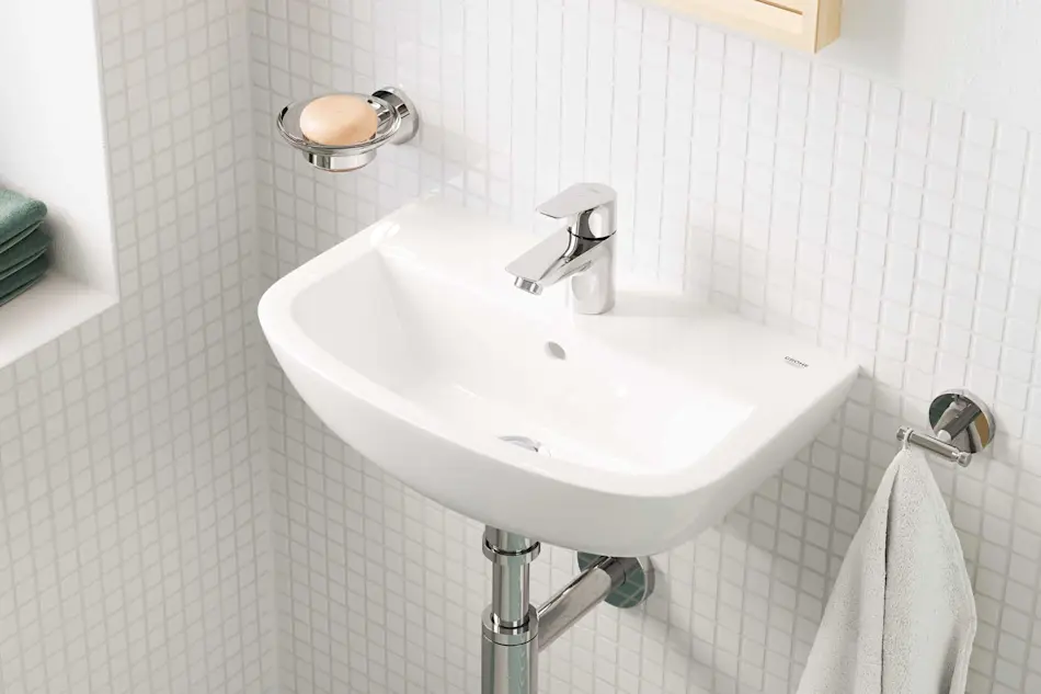 White bathroom sink with chrome faucet mounted on white tiled wall, soap dish and towel holder visible.
