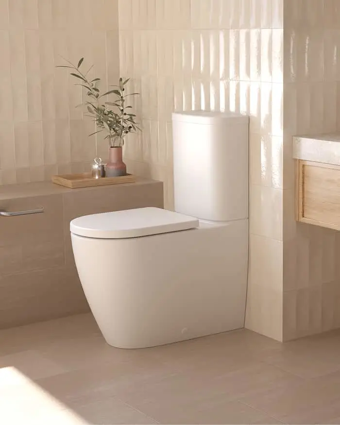 Modern white toilet in a beige bathroom with vertical tile walls, small potted plant on wooden shelf nearby.