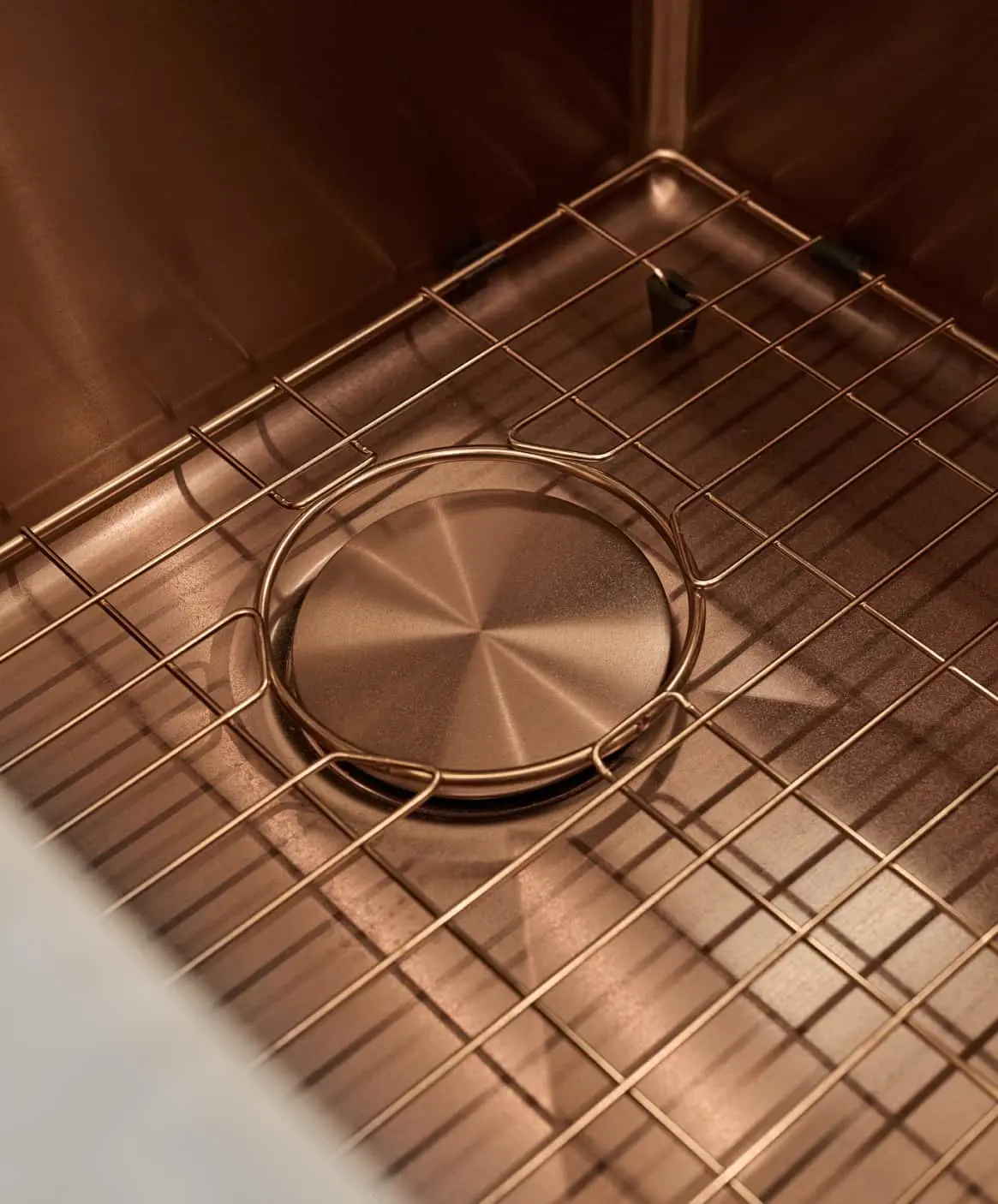 Copper sink with metal grid rack and circular drain cover, showing warm metallic tones in kitchen installation.