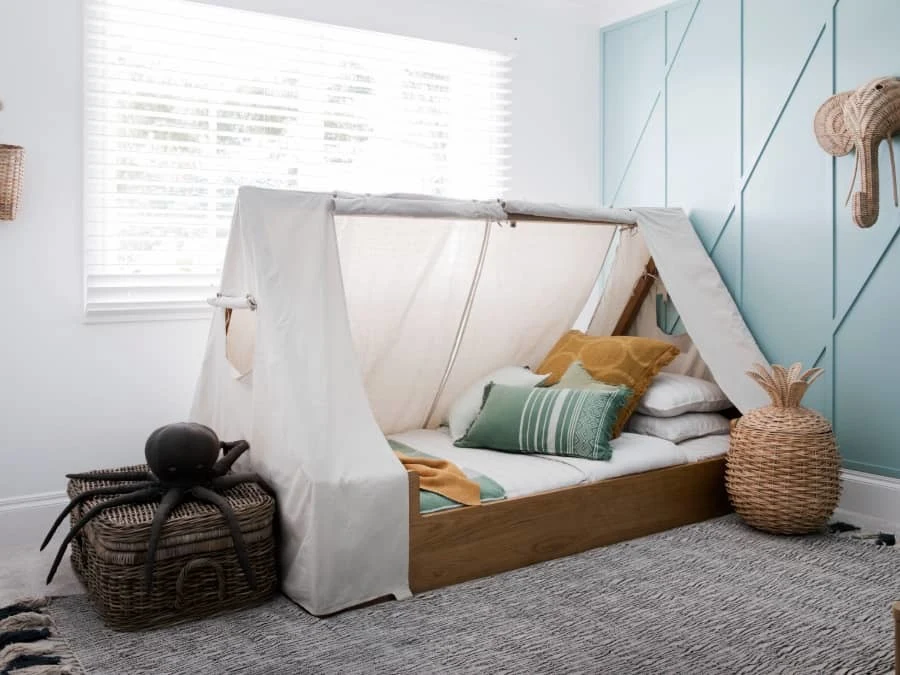 Children's tent bed with white canopy, colorful pillows, and wicker baskets in a room with light blue walls and window.