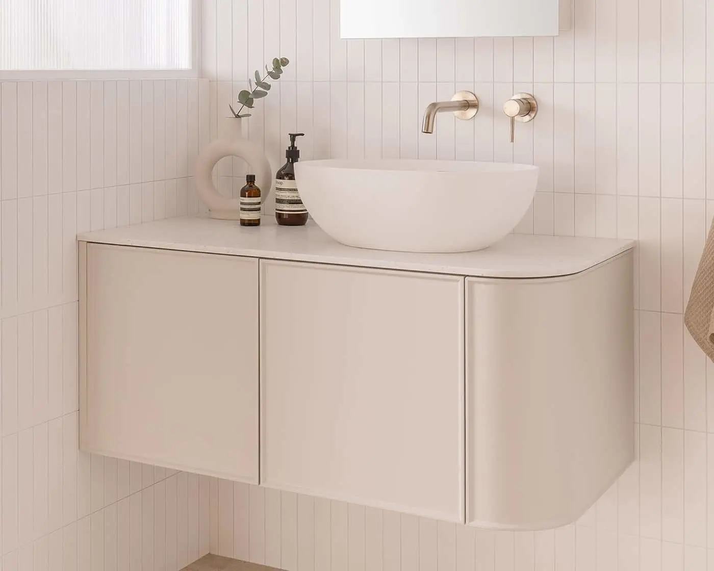 Modern bathroom vanity with white vessel sink, brass wall-mounted faucet, and minimalist decor on cream cabinetry.