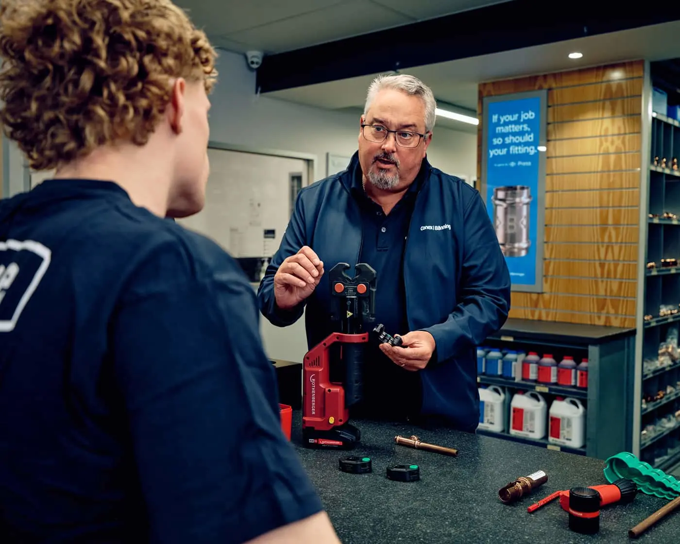 Instructor demonstrating plumbing tools to a student at a Reece Plumbing counter with equipment.