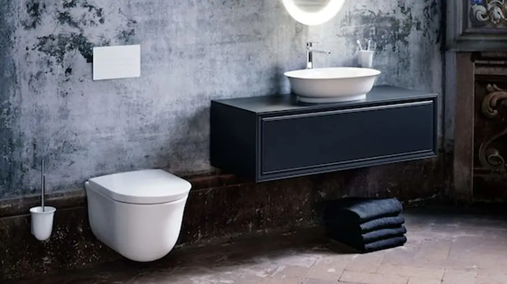 Modern bathroom with concrete walls, white toilet, black vanity with vessel sink, and folded dark towels on the floor.