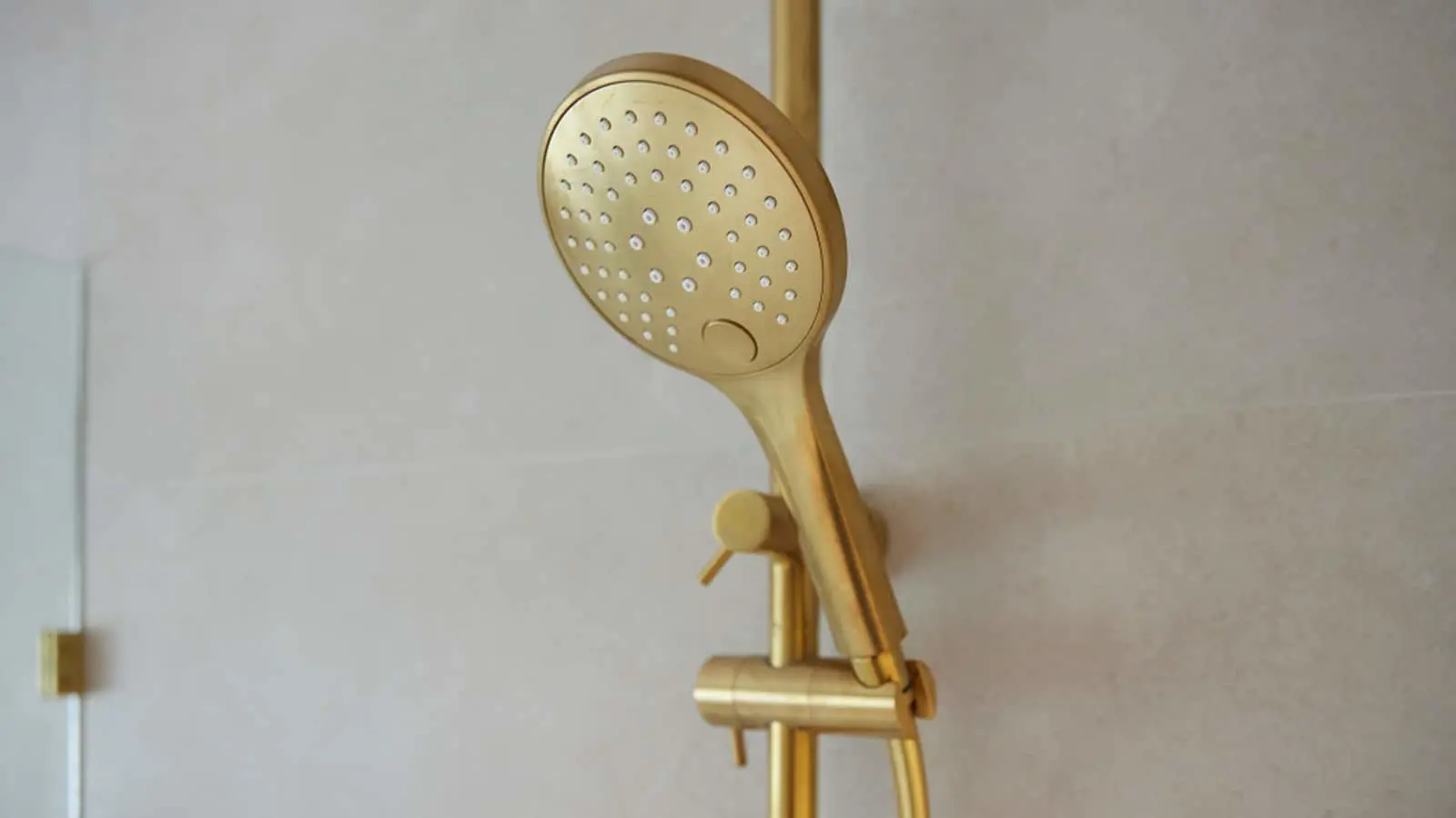 Gold handheld shower head mounted on a white bathroom wall with multiple water spray holes.
