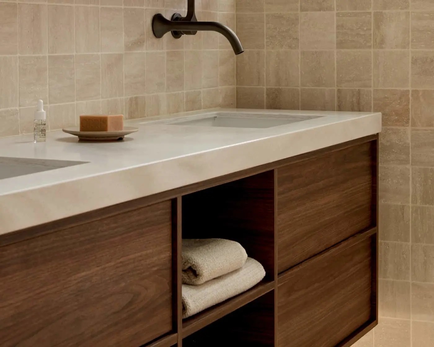 Modern bathroom vanity with white countertop, wooden cabinets, folded towels, and wall-mounted bronze faucet.