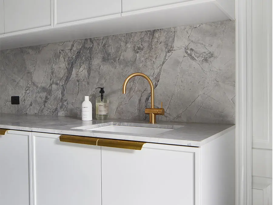 Modern kitchen sink with gold faucet, white cabinets, and gray marble backsplash with two soap dispensers.
