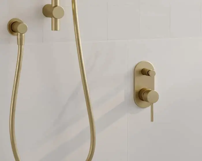 Modern brass shower fixtures with handheld sprayer mounted on white tiled wall.
