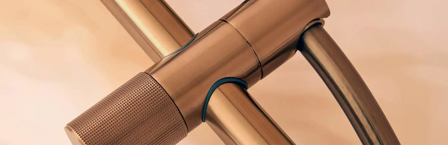 Close-up of bronze plumbing fixture with textured grip and connecting pipes against beige background.