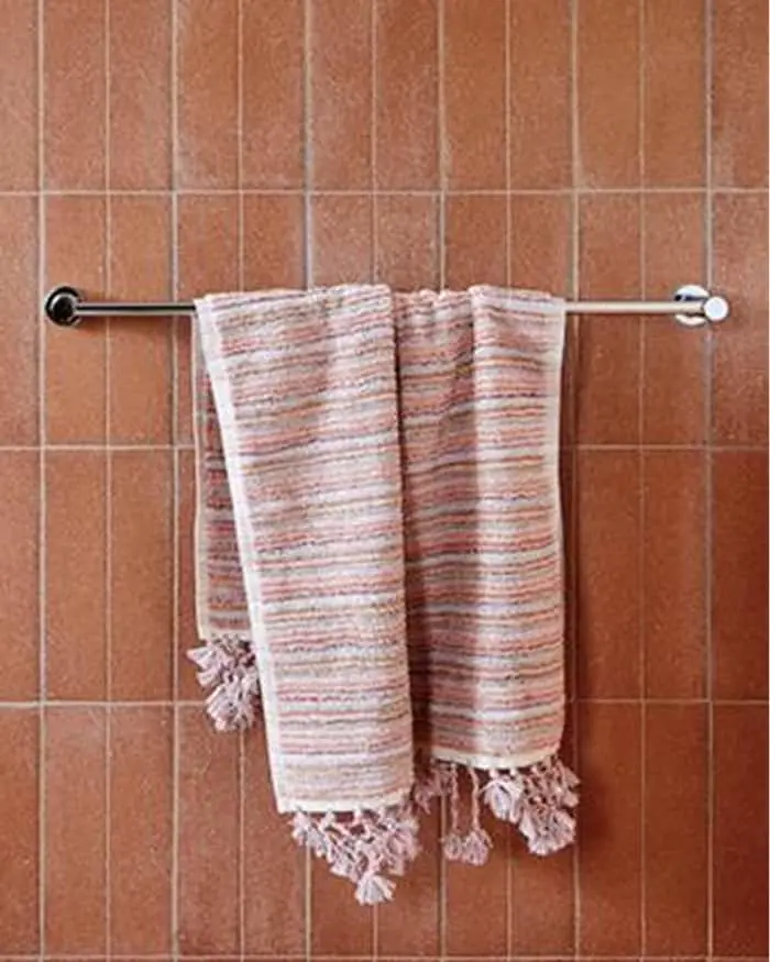 Striped towel with tassels hanging on a metal towel bar against terracotta tiled bathroom wall.