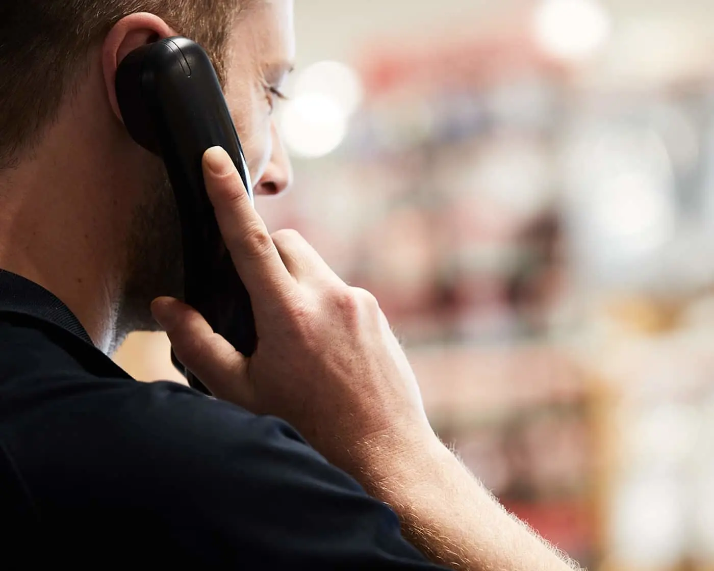 Person in dark clothing holding a black telephone receiver to their ear with blurred background.