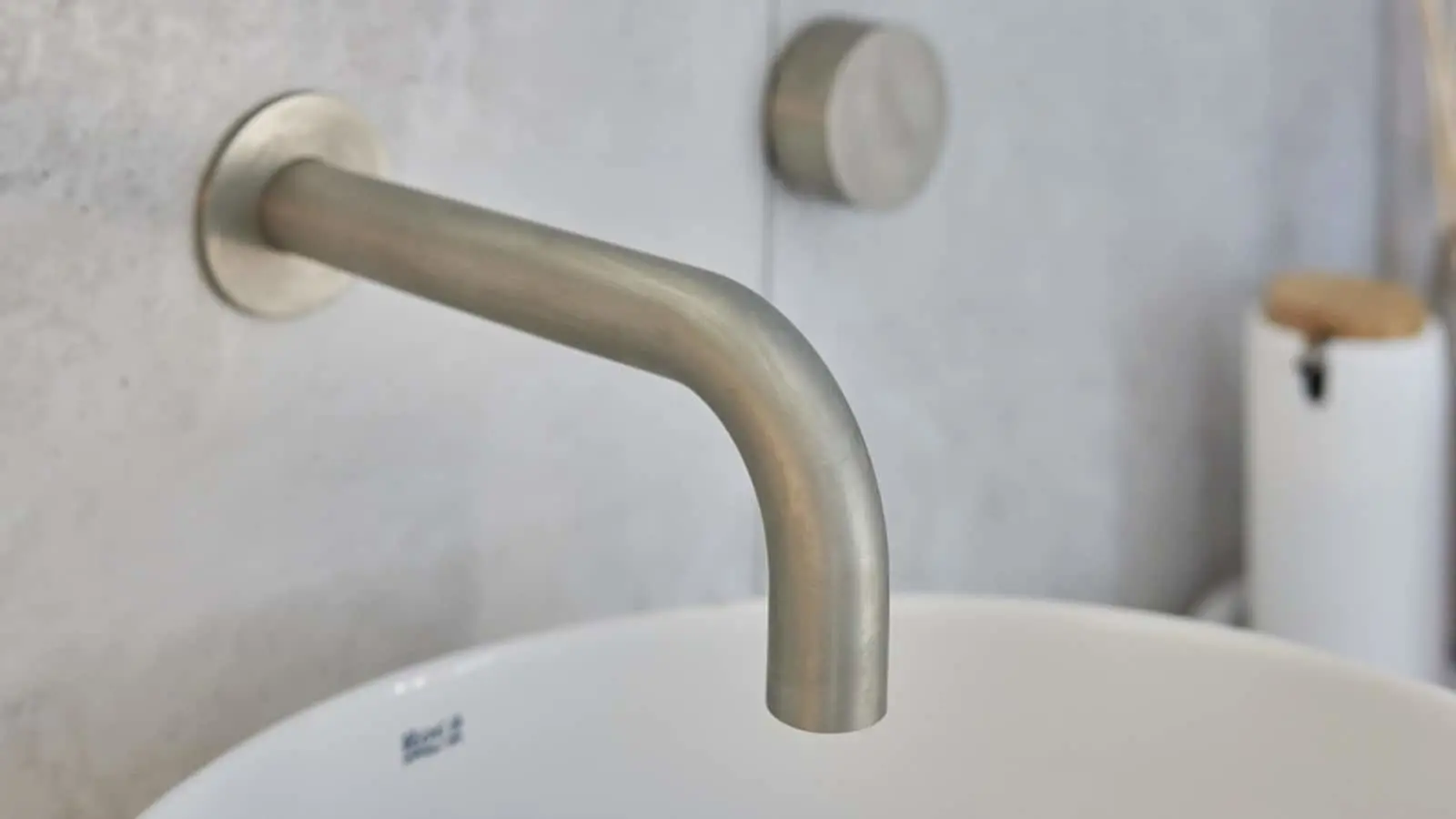 Modern brushed nickel wall-mounted bathroom faucet with curved spout above a white sink basin.