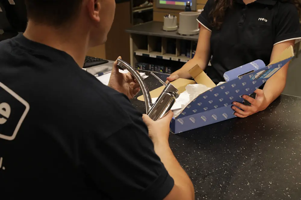 Store employee showing a customer a chrome faucet while packaging sits on the counter.