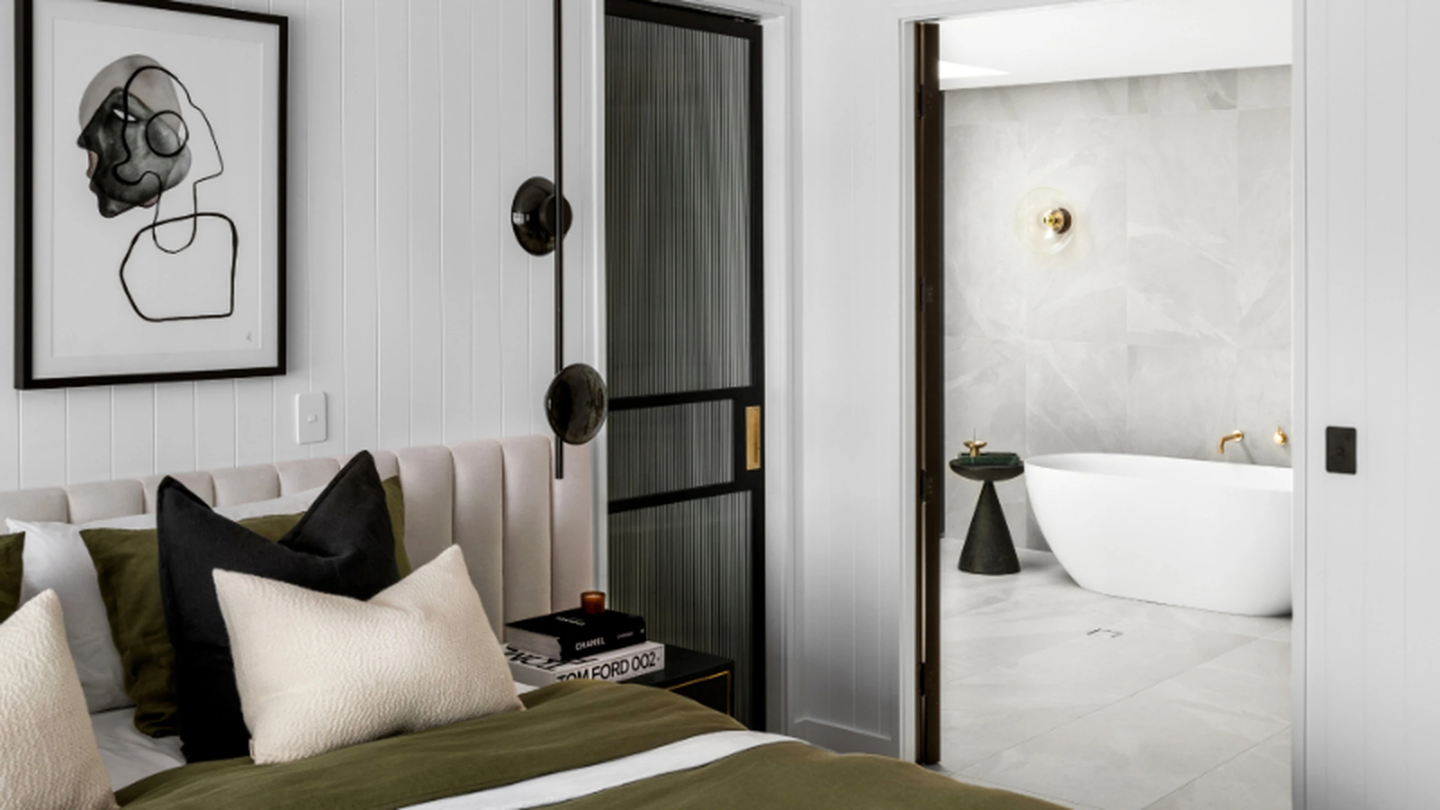Modern bedroom with olive green bedding, abstract wall art, and view into marble bathroom with freestanding tub.
