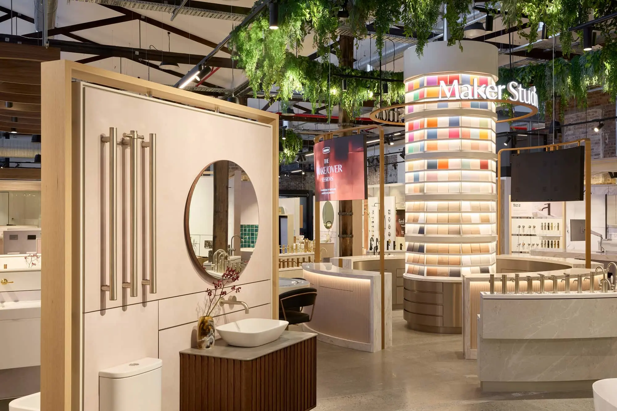 Interior of a bathroom products showroom with displays, a colorful tile column labeled Maker Studio, and hanging greenery.