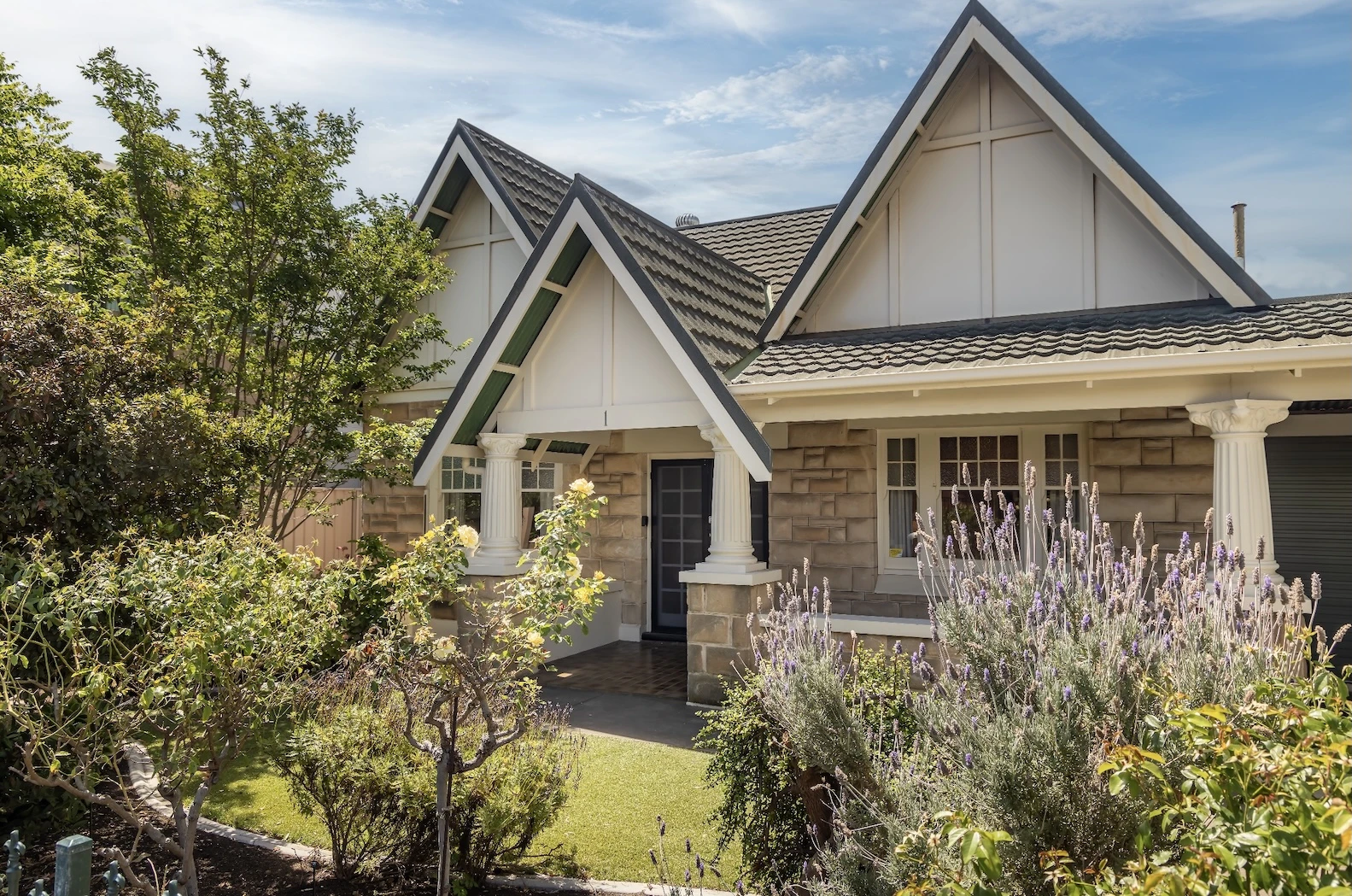 Suburban house with steep gabled roofs, stone accents, and landscaped garden featuring lavender plants.
