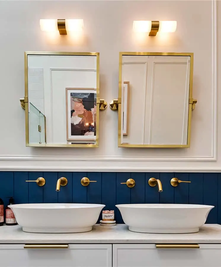 Modern bathroom with dual white vessel sinks, gold-framed mirrors, brass fixtures, and navy blue accent wall.