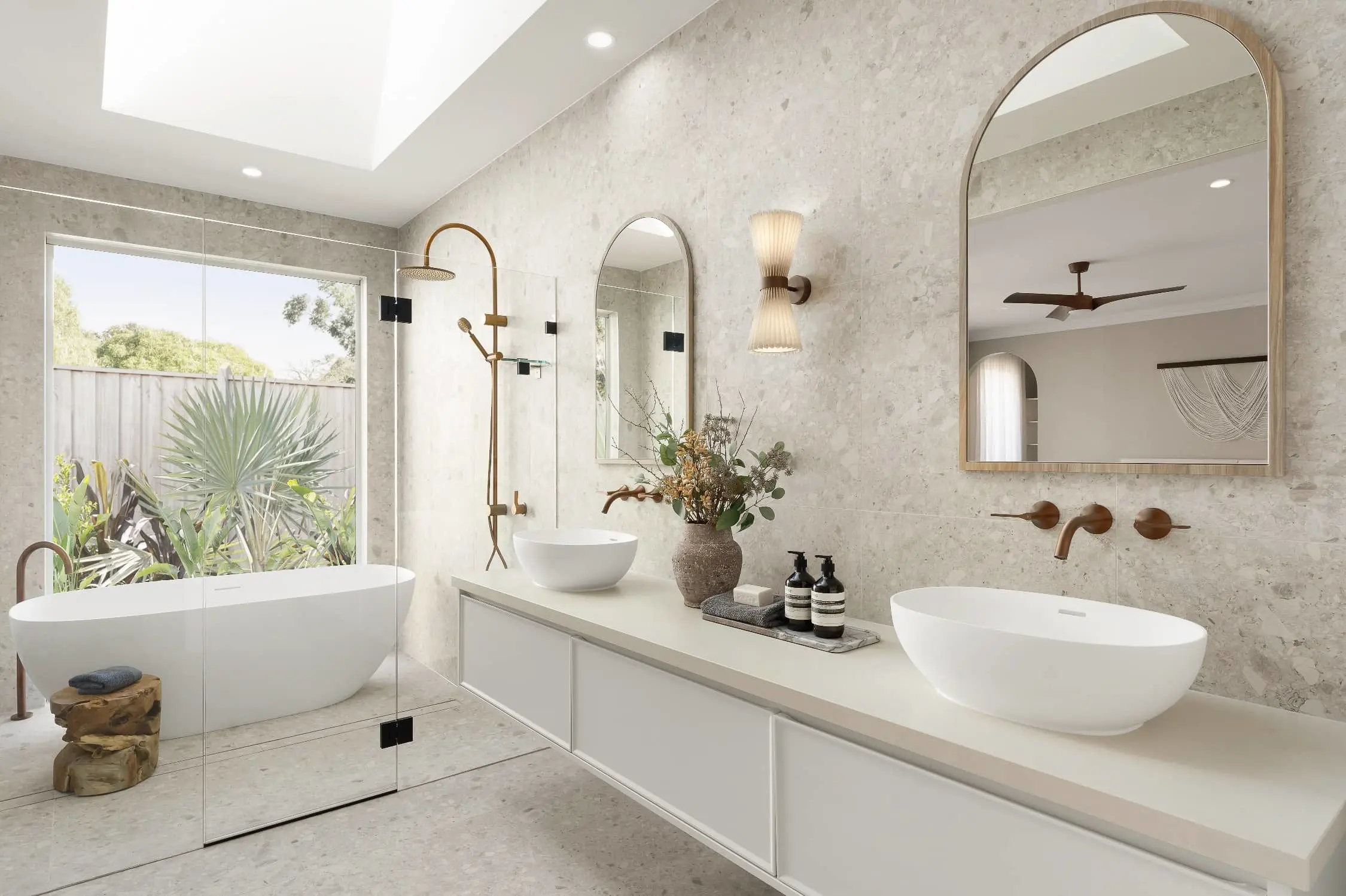 Modern luxury bathroom with marble walls, white vessel sinks, freestanding tub, gold fixtures, and garden view window.