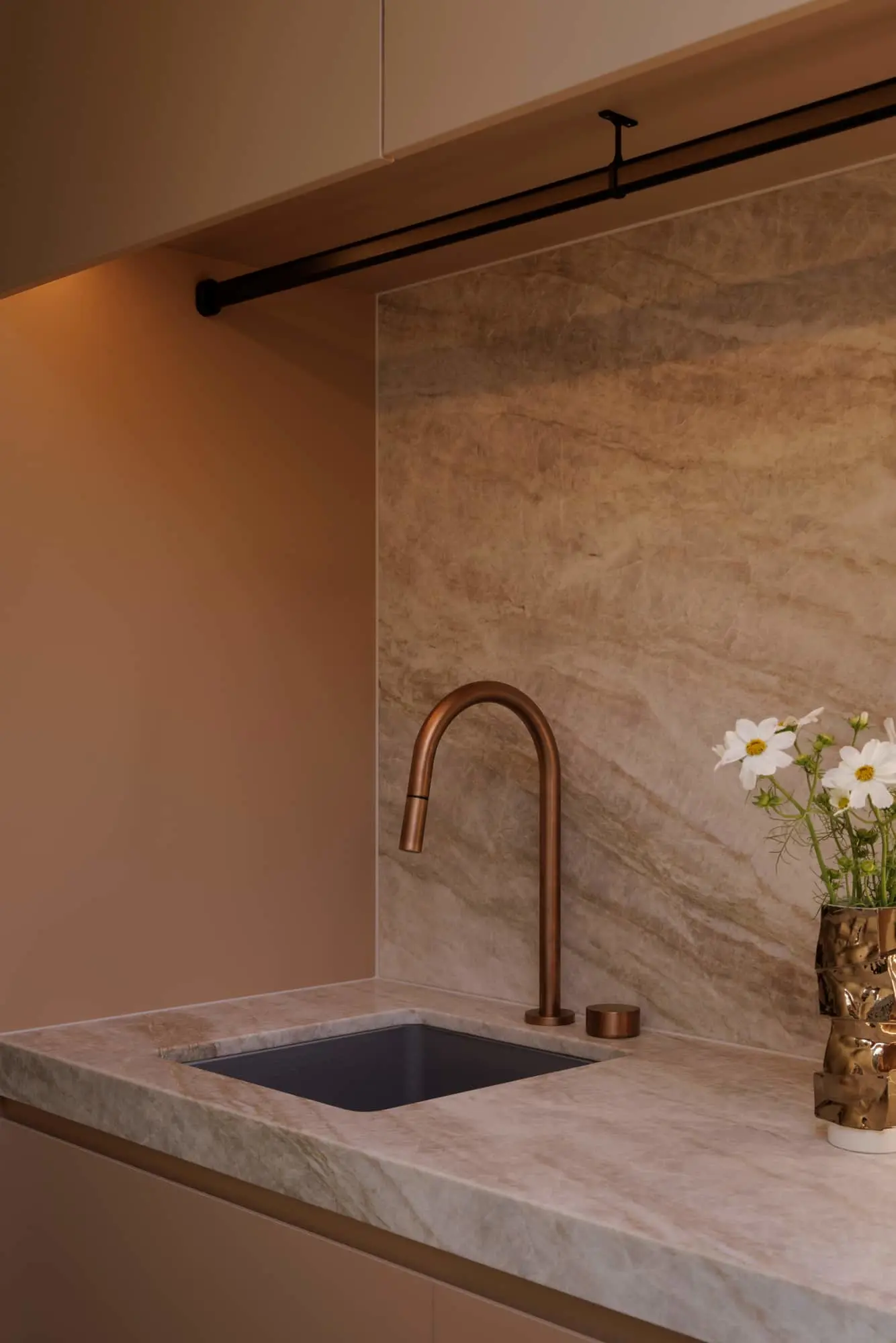 Modern kitchen sink with copper faucet, marble countertop and backsplash, and white flowers in a bronze vase.
