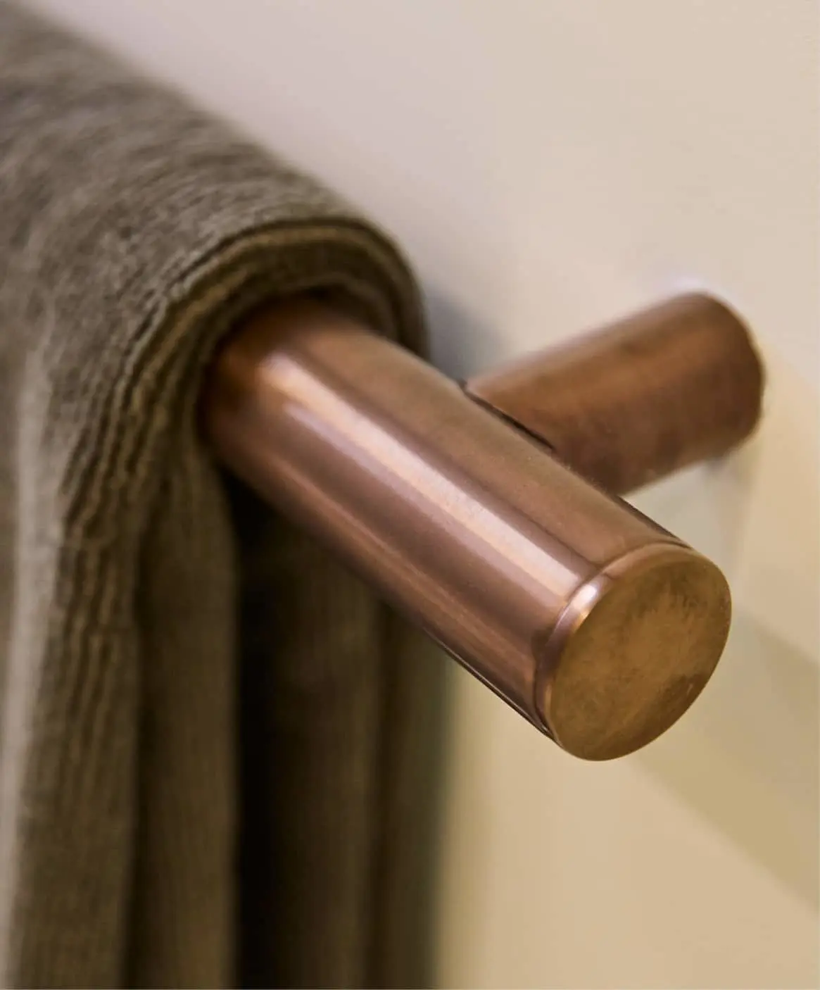 Gray fabric towel or blanket hanging on a bronze rod mounted to a light-colored wall.