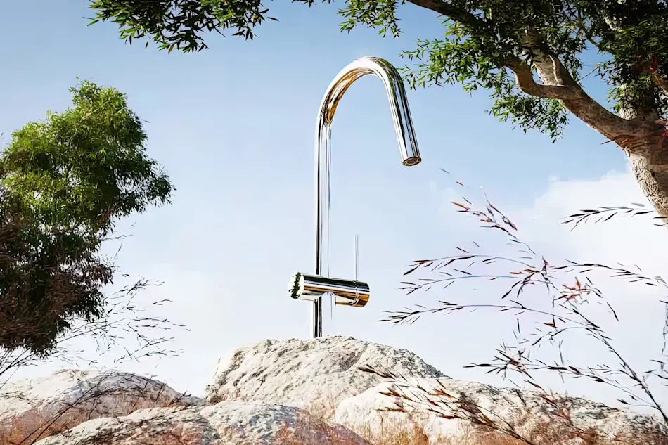 Modern chrome outdoor faucet mounted on stone, surrounded by trees and grasses against a blue sky.