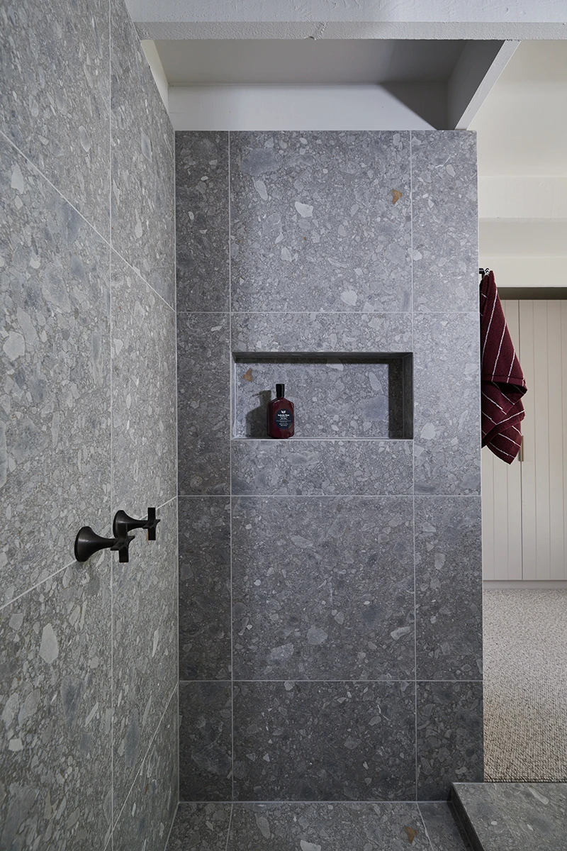 Modern bathroom with gray terrazzo tile walls, built-in shower niche holding a bottle, and burgundy towel hanging nearby.